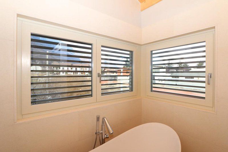 Bagno ad angolo con persiane bianche in stile coloniale su tre finestre sopra la vasca da bagno
