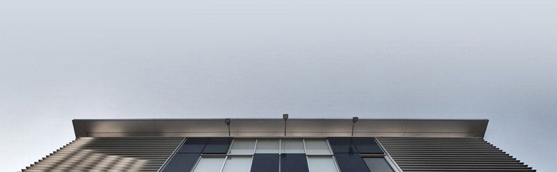 Vista dal basso della facciata di un edificio moderno con finestre riflettenti e tetto metallico contro il cielo.
