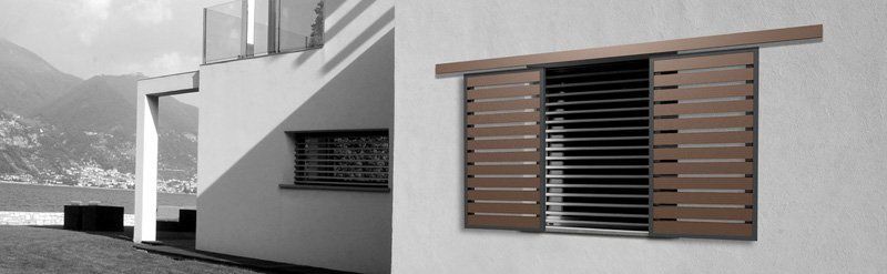 Esterno di una casa moderna con pareti bianche, una finestra stretta e una persiana a lamelle di legno.