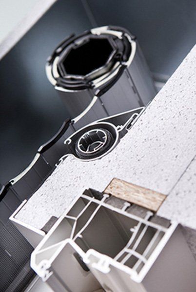 Primo piano di un orologio da parete analogico nero su una superficie bianca ruvida, con una cornice geometrica bianca sottostante.