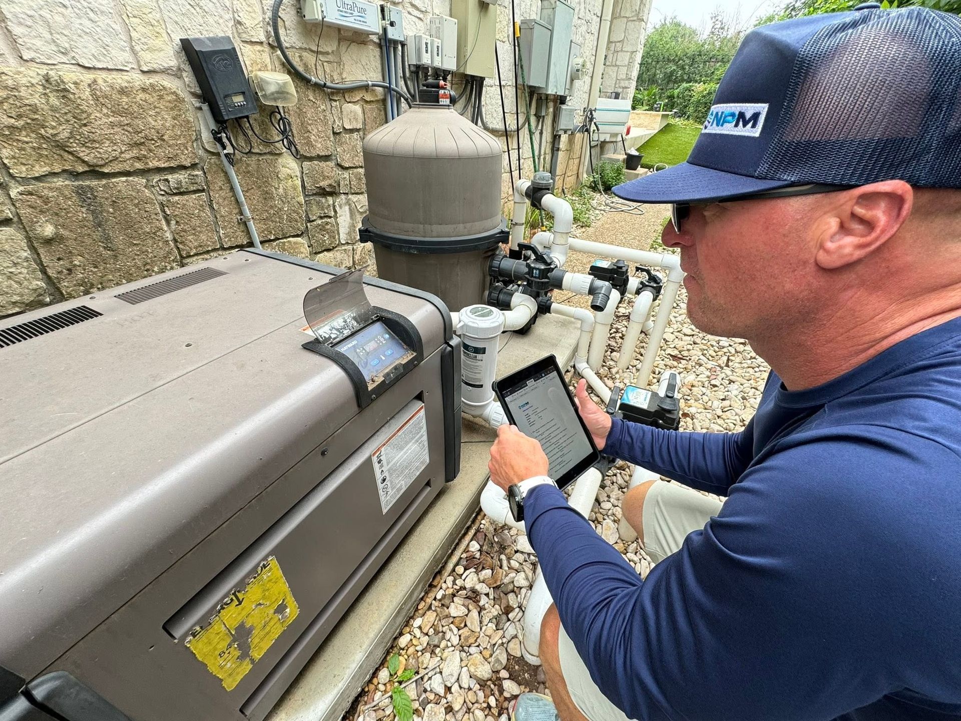Technician inspecting outdoor pool equipment with a tablet beside a house wall