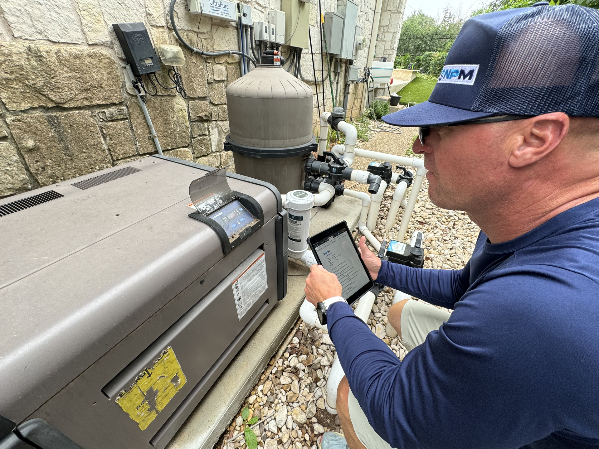 Technician inspecting outdoor HVAC unit with a tablet beside a stone wall