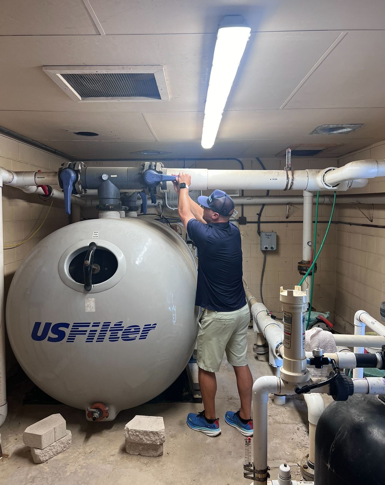 Worker adjusting pipes beside a large round water tank in a utility room