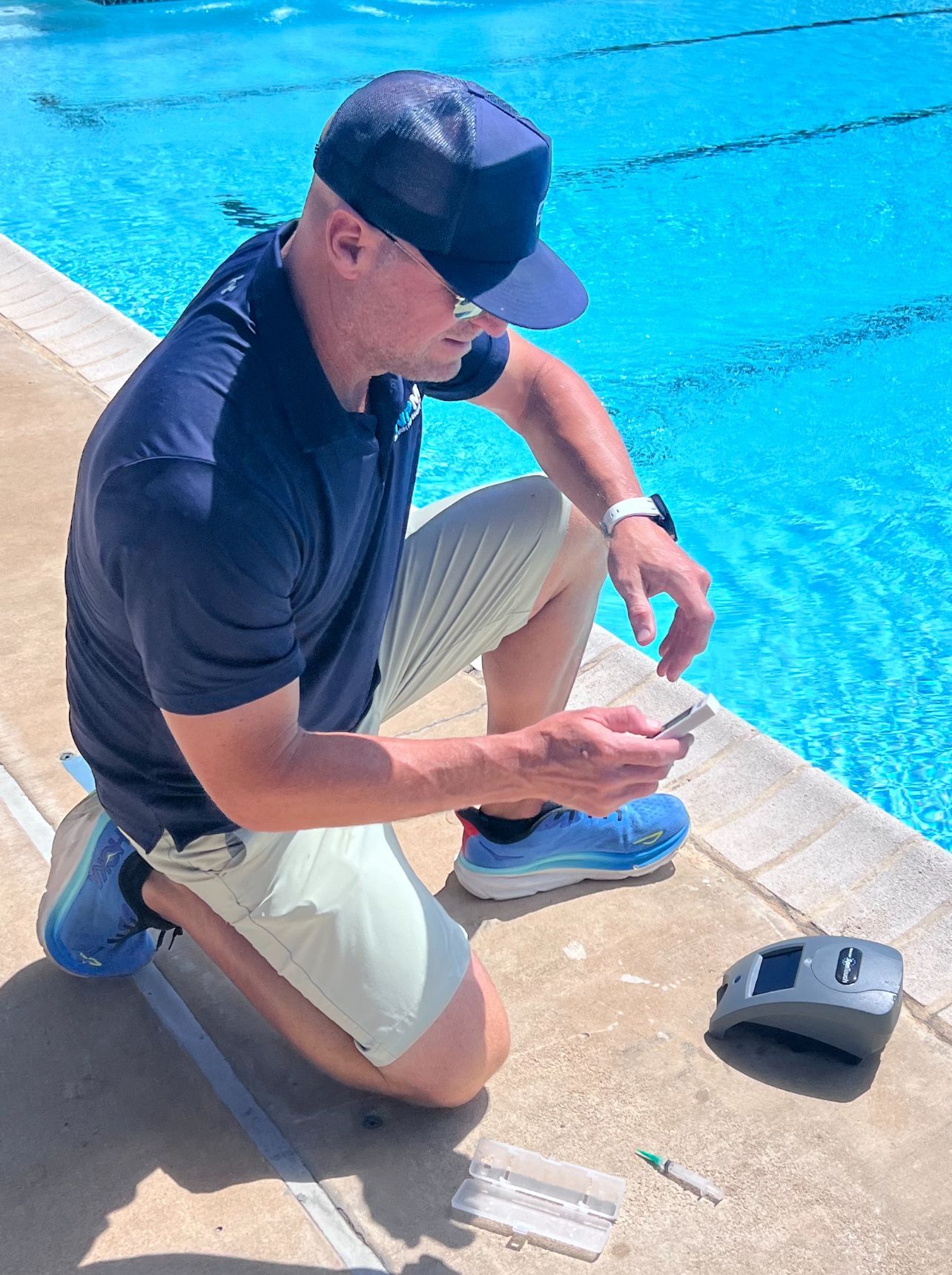 Person kneeling by a pool, using a small device near the water’s edge