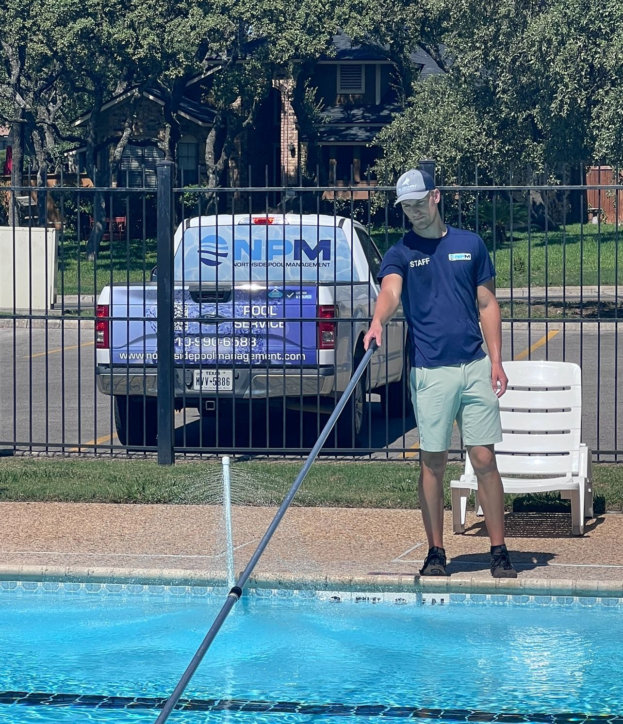 Man using a pole to clean debris from a swimming pool beside the deck