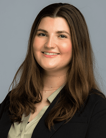 Smiling professional in a black blazer and light blouse against a gray background
