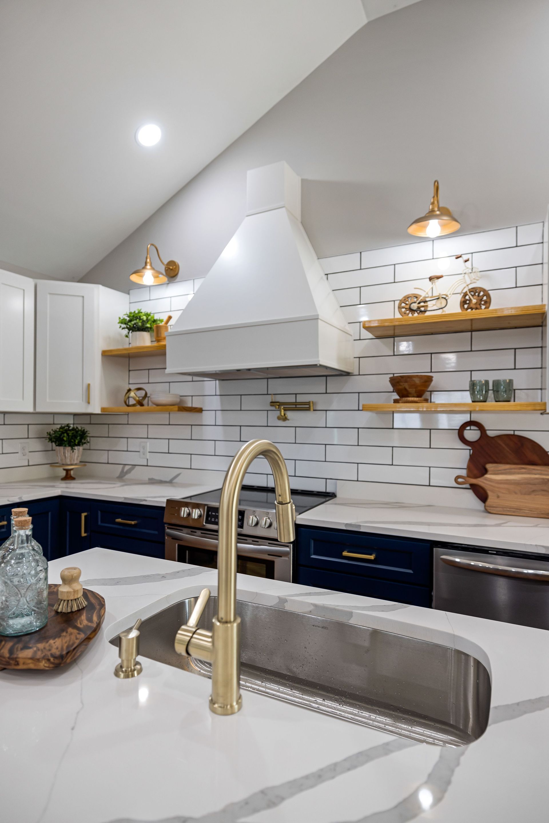 Bright modern kitchen with white tile backsplash, gold fixtures, and dark blue cabinets.
