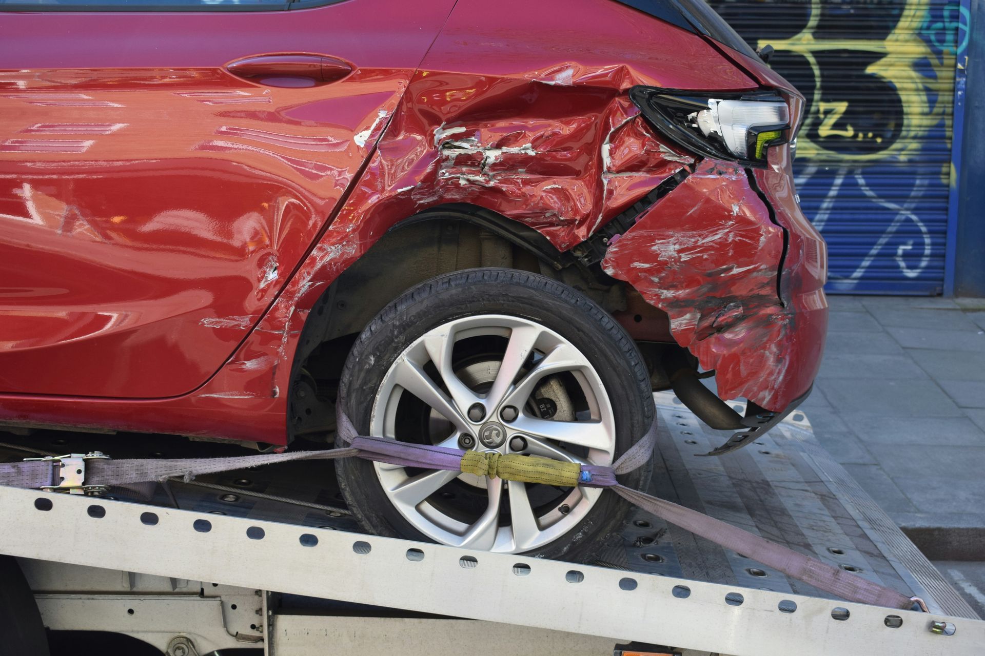 Red car with severe damage to the rear, loaded on a tow truck.