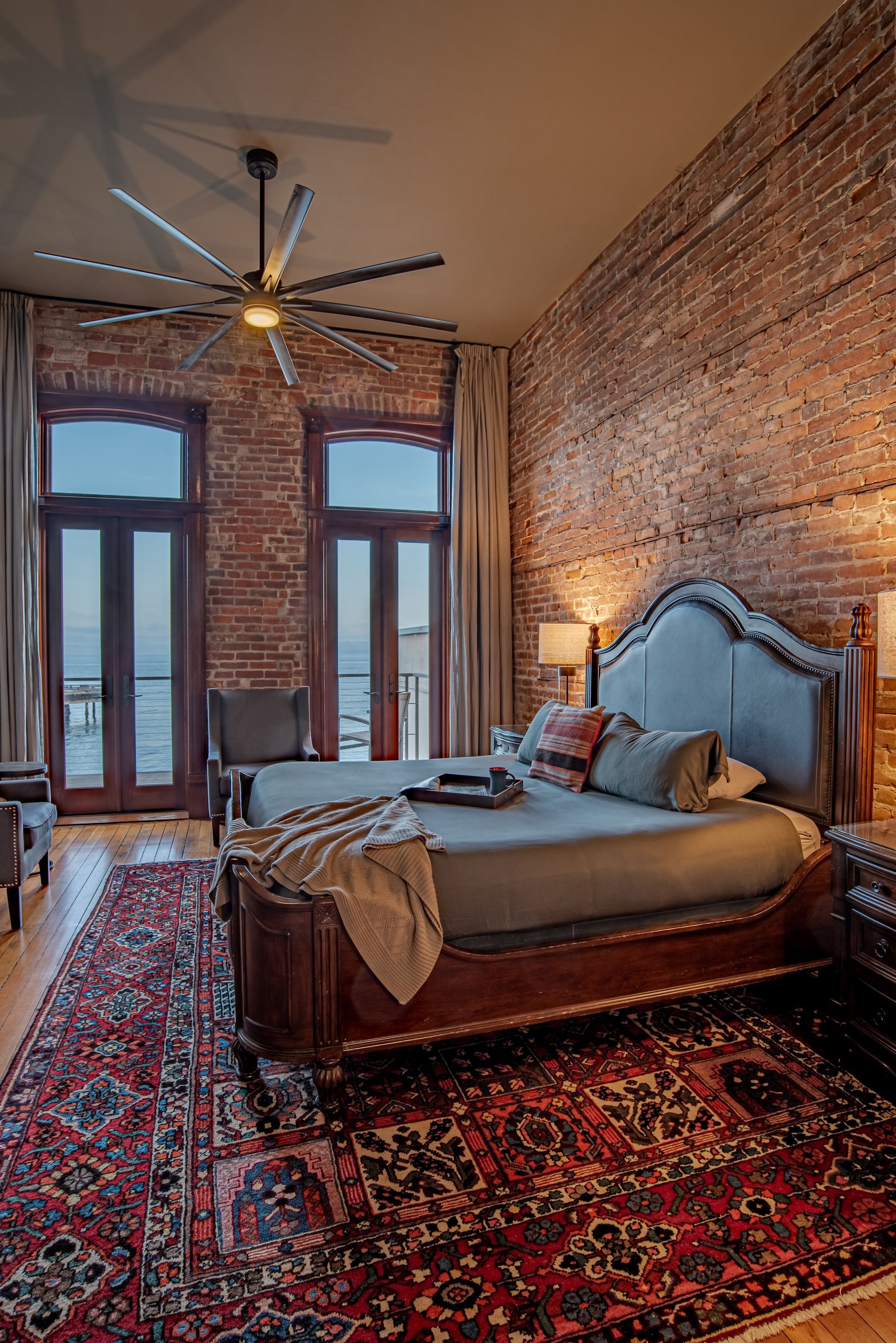 A bedroom with a bed , rug , ceiling fan and brick walls.