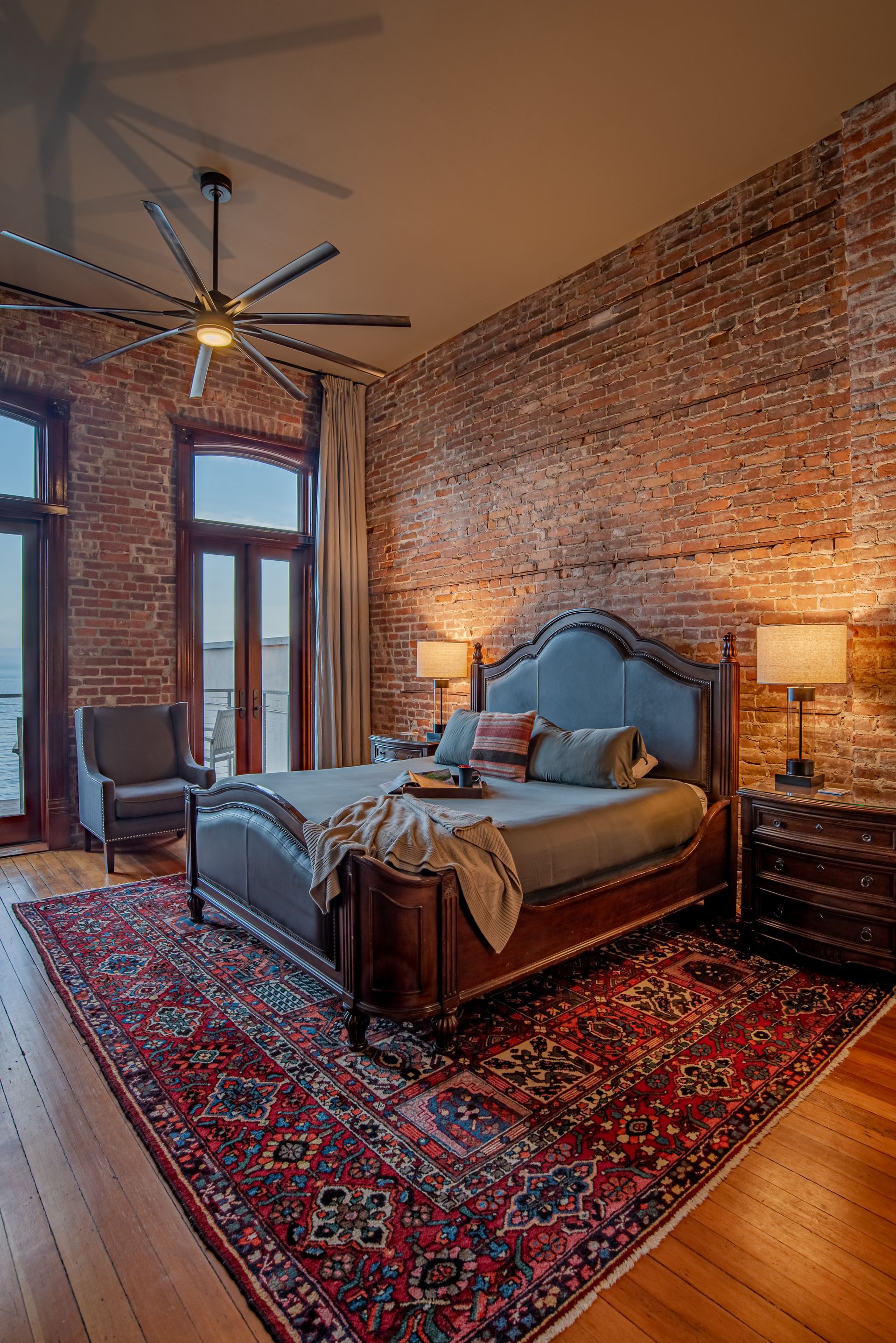 A bedroom with a bed , rug , ceiling fan and brick walls.