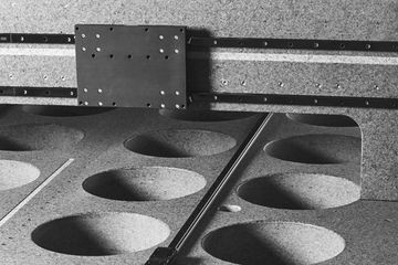 Close-up of a CNC machine bed with a grid of circular indentations and a linear rail mechanism with a mounting plate.