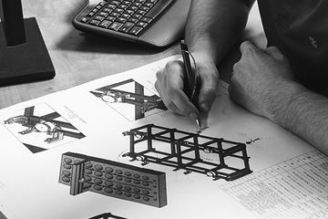 A person sketching technical engineering designs of a structural frame and components on a large sheet of paper.