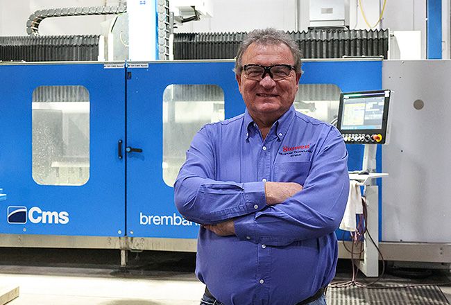 Male worker in blue button-up wearing safety glasses while posing in front of blue machine