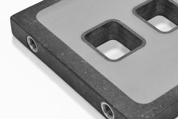 A close-up of a rectangular, dark textured industrial plate with two inset square openings and two threaded metal ports.