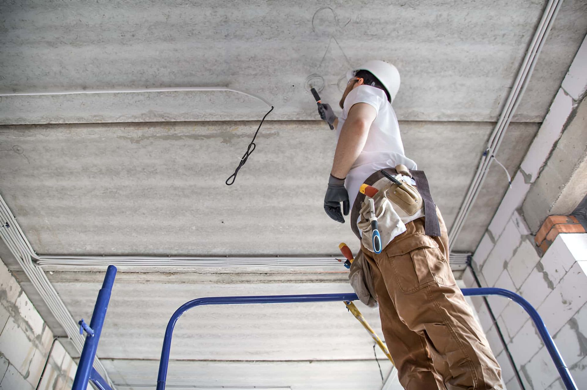 A Man Is Standing On A Ladder Working On A Ceiling — Homeland Electrical & Refrigeration In Braitling, NT