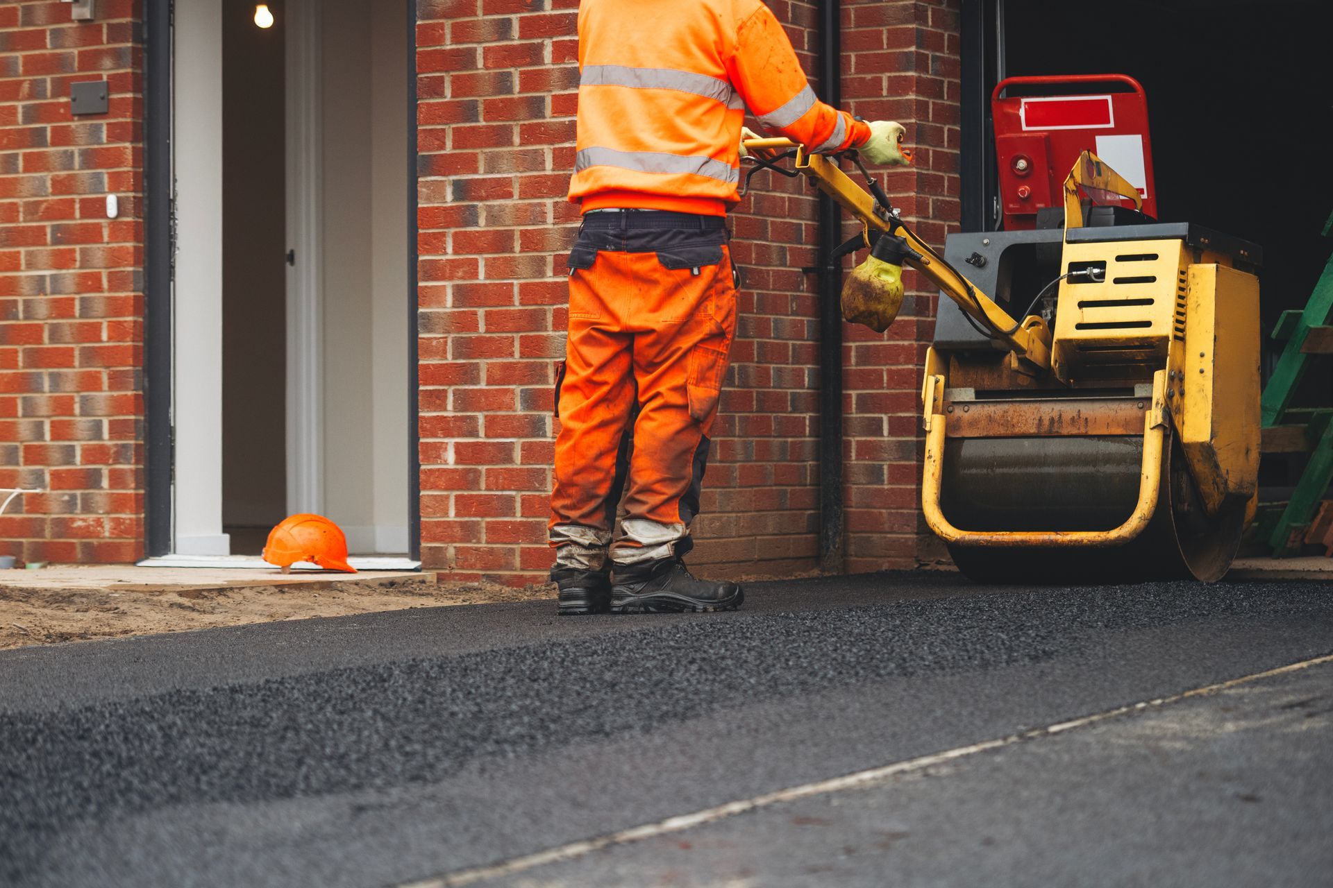 Construction worker applying asphalt in residential area private parking spot driveway.