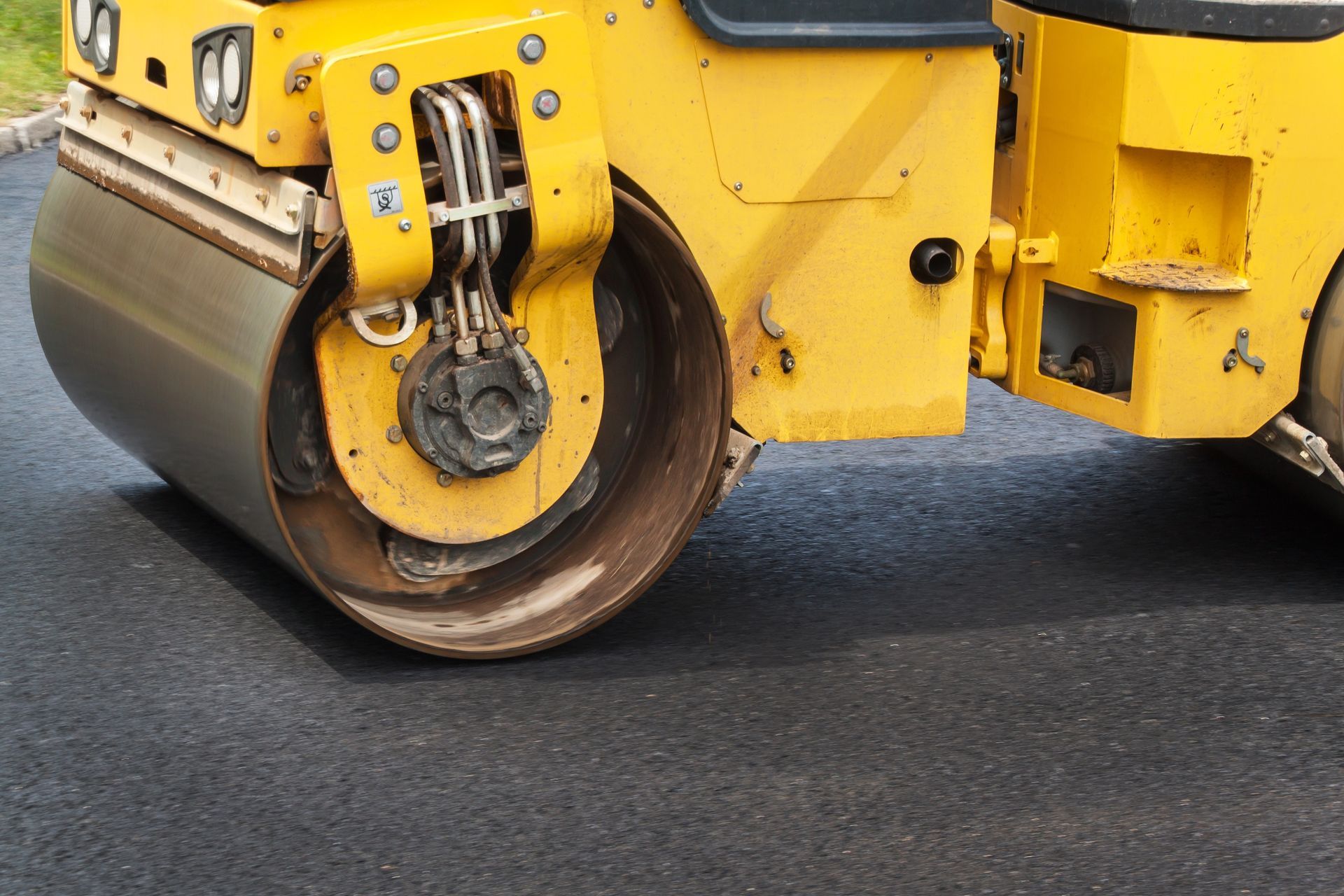 Yellow road roller compacting freshly laid asphalt on a roadway during paving operations. Yellow road roller compacting freshly laid asphalt on a roadway during paving operations.