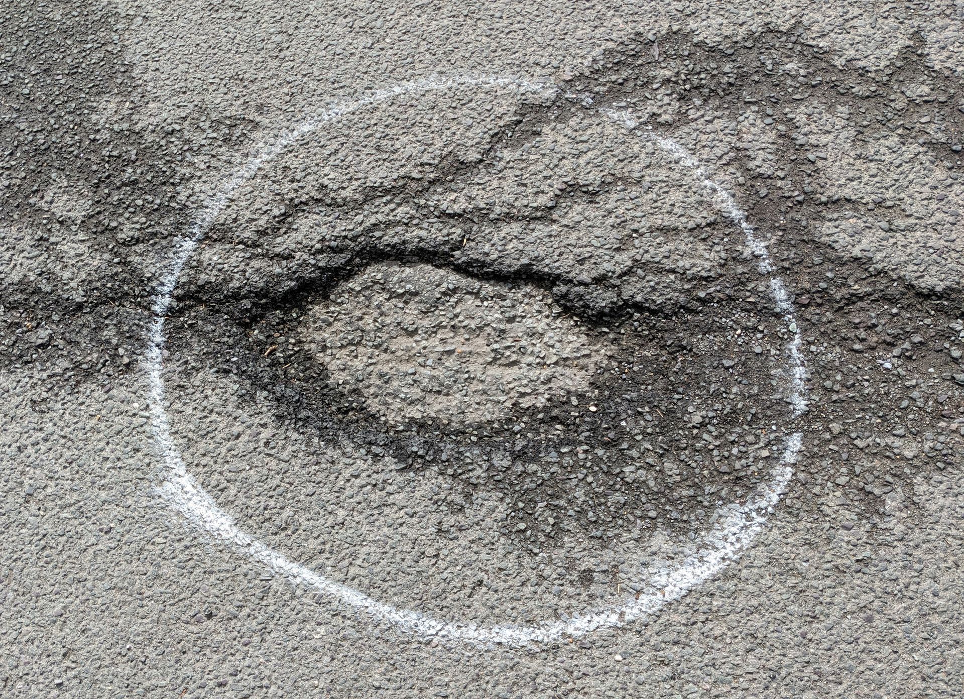 White circle drawn around a damaged area of cracked asphalt.