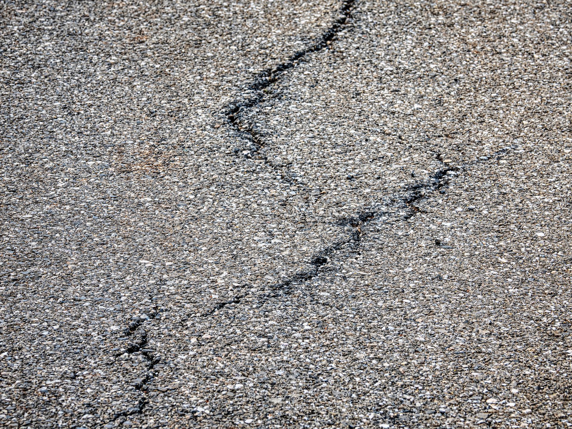 Cracked asphalt pavement with irregular, dark fissure running across the surface.
