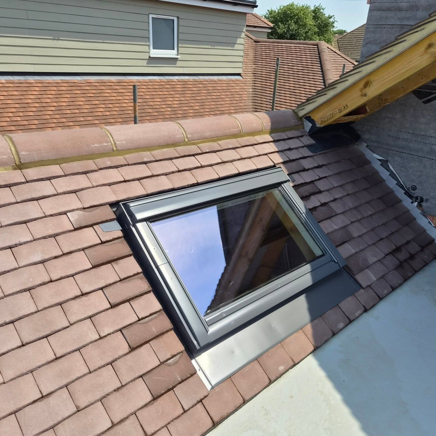 Open skylight window set into a sloped shingle roof beside a brick house wall.