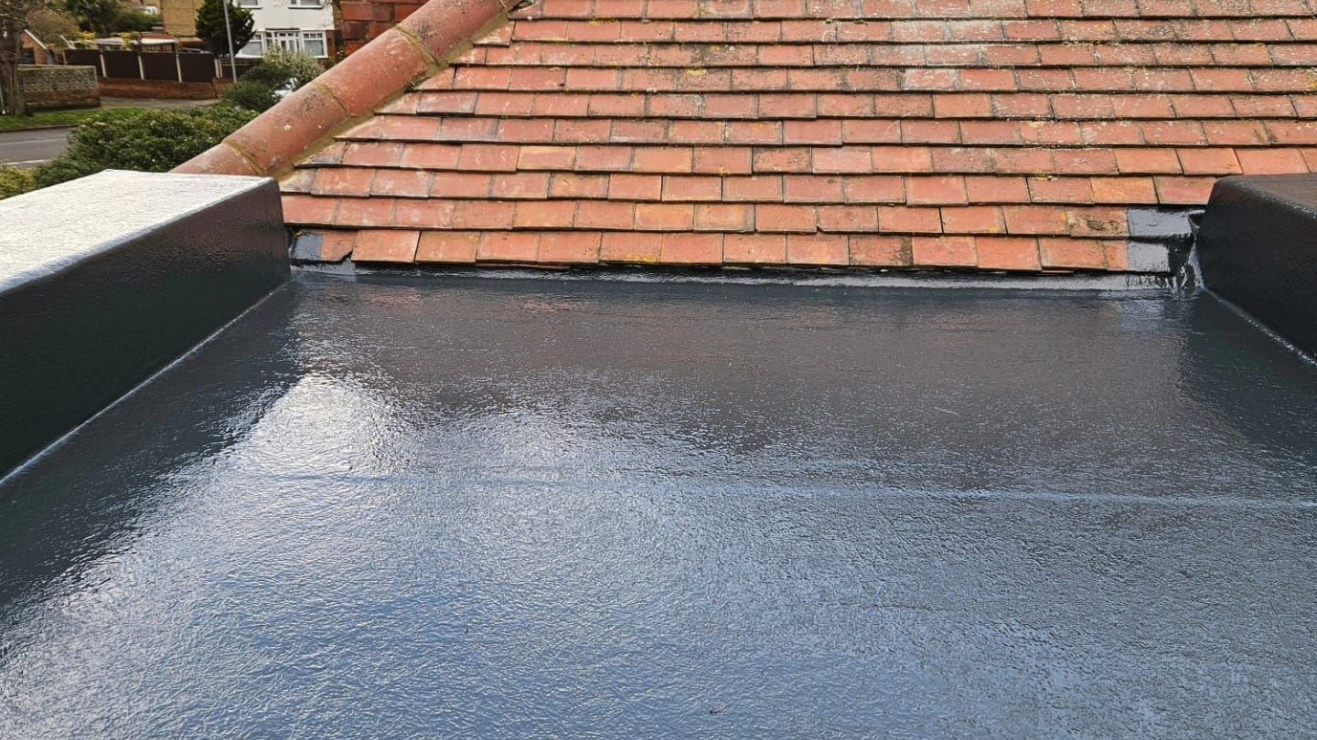 A black flat roof with a brick tiled roof in the background.