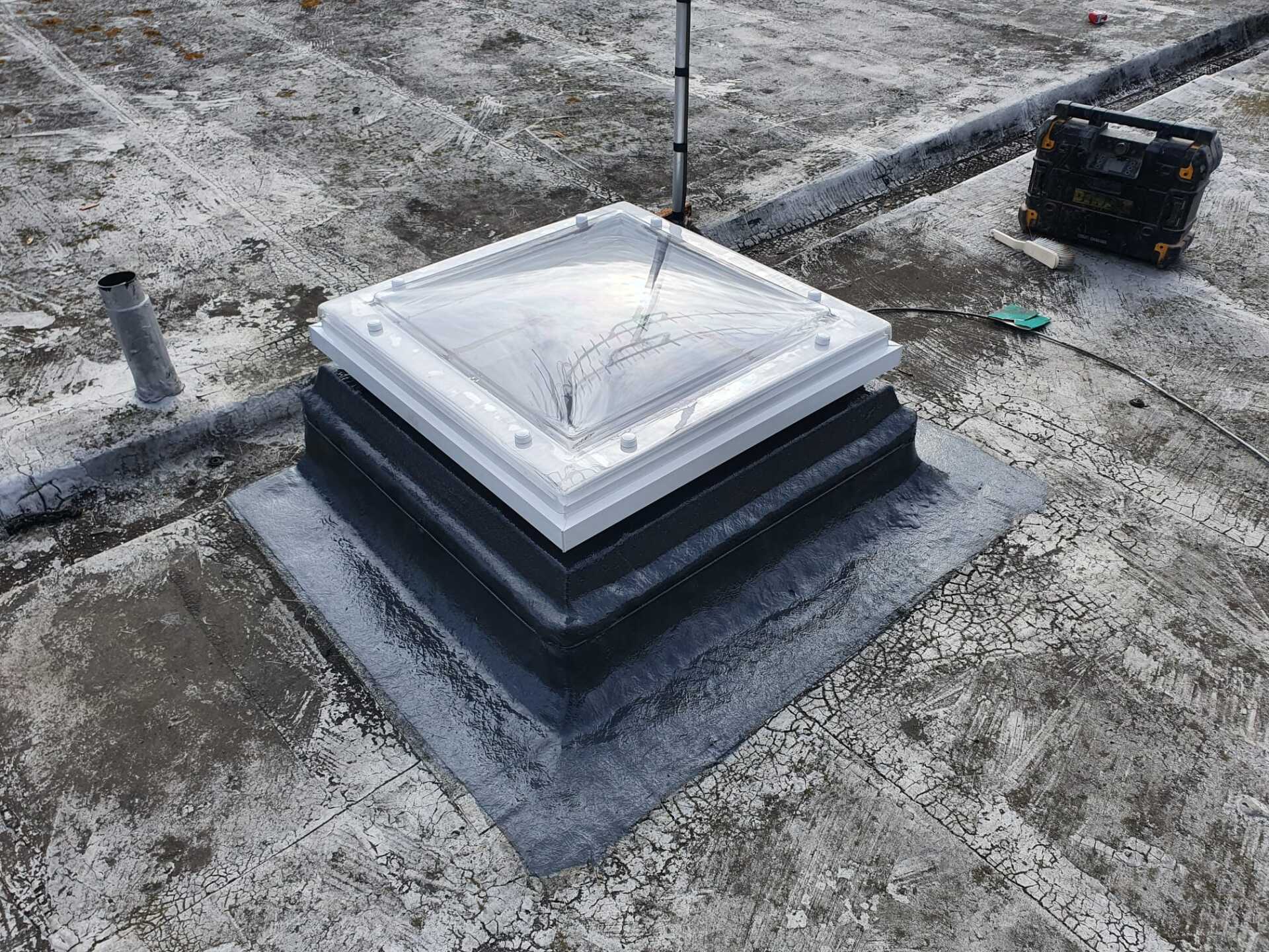 a square skylight is sitting on top of a concrete roof .