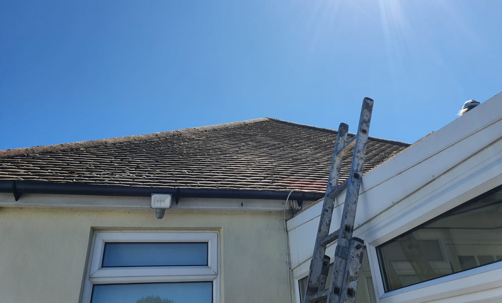 Residential roof with red chimney and ladder under sunny and clear sky.