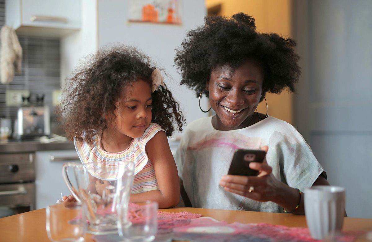 A woman is holding a girl and looking at her phone