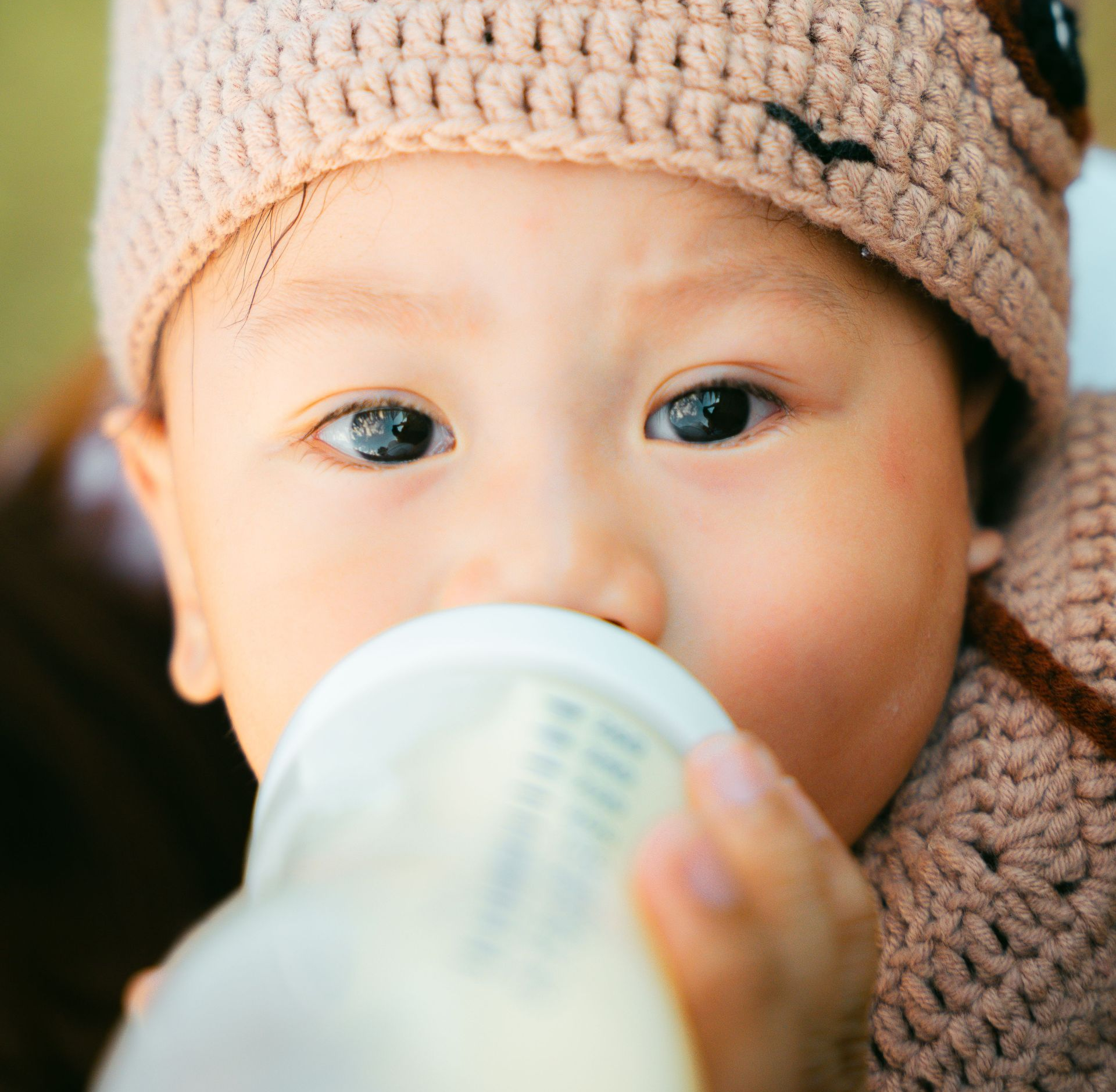Baby drinking from a bottle while being held close, with a pink blanket visible.