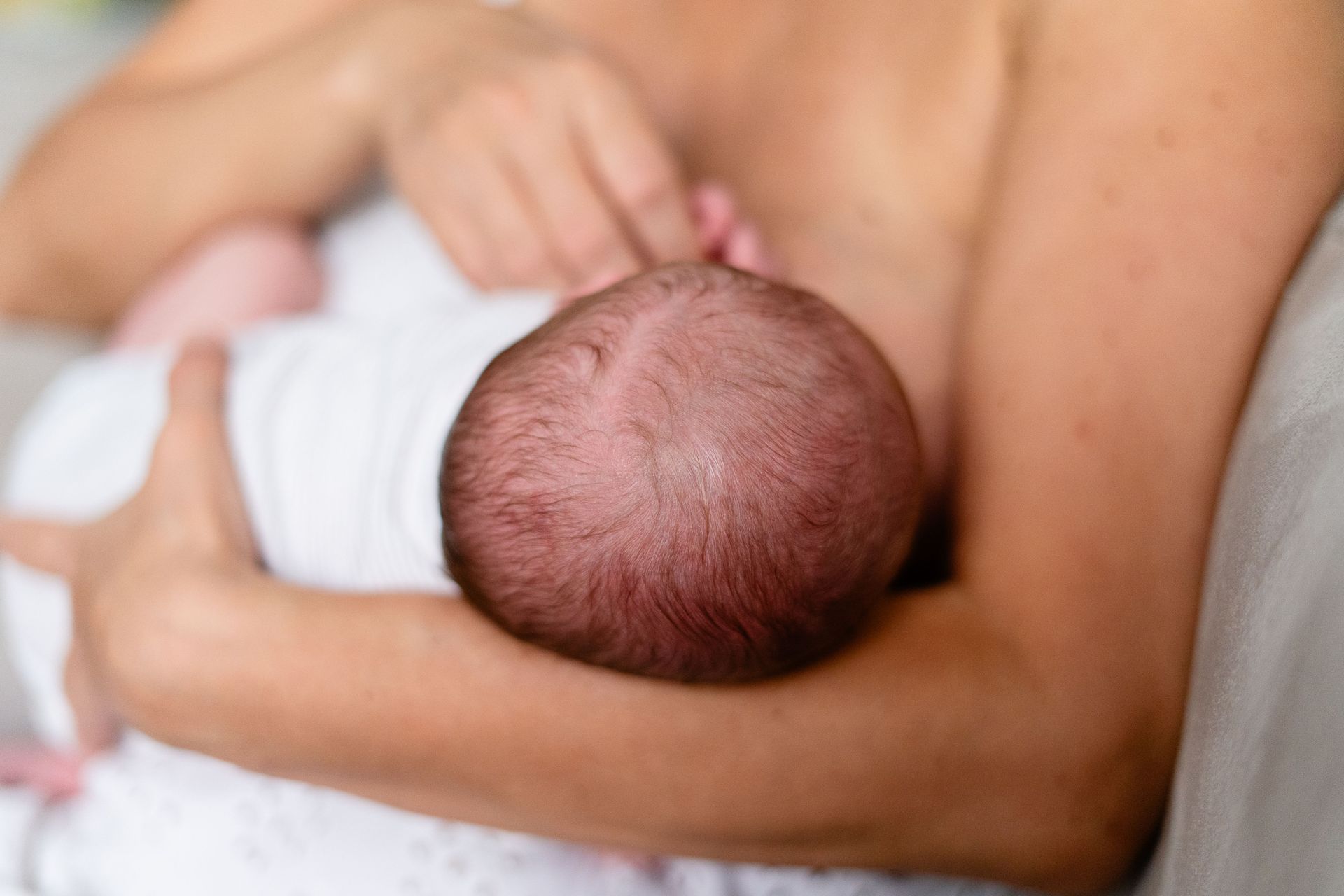 Baby being breastfed in a caregiver’s arms, close-up on the infant’s head and body