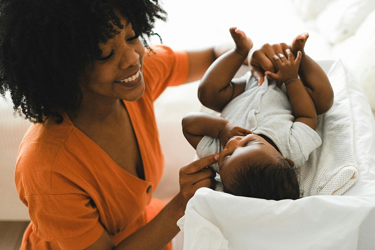 Woman in orange shirt smiling and holding a baby on a white bed