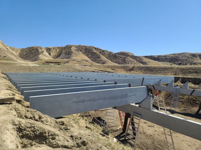 Solar panel installation in progress, with rows of metal frames on a hillside under a blue sky.