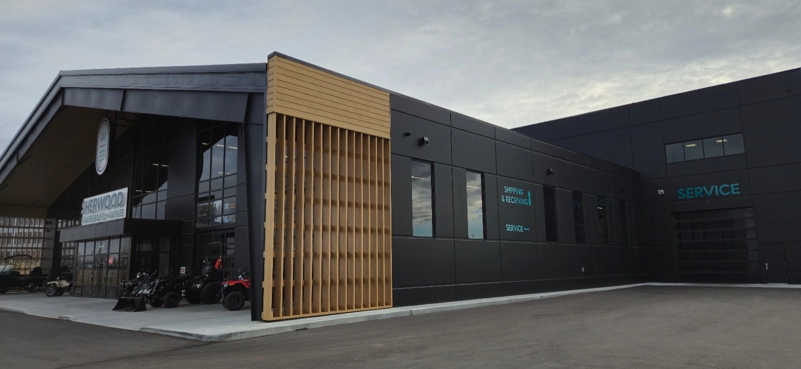 Modern dark building with wooden accents. The building has large windows and an overhang, with vehicles parked outside.