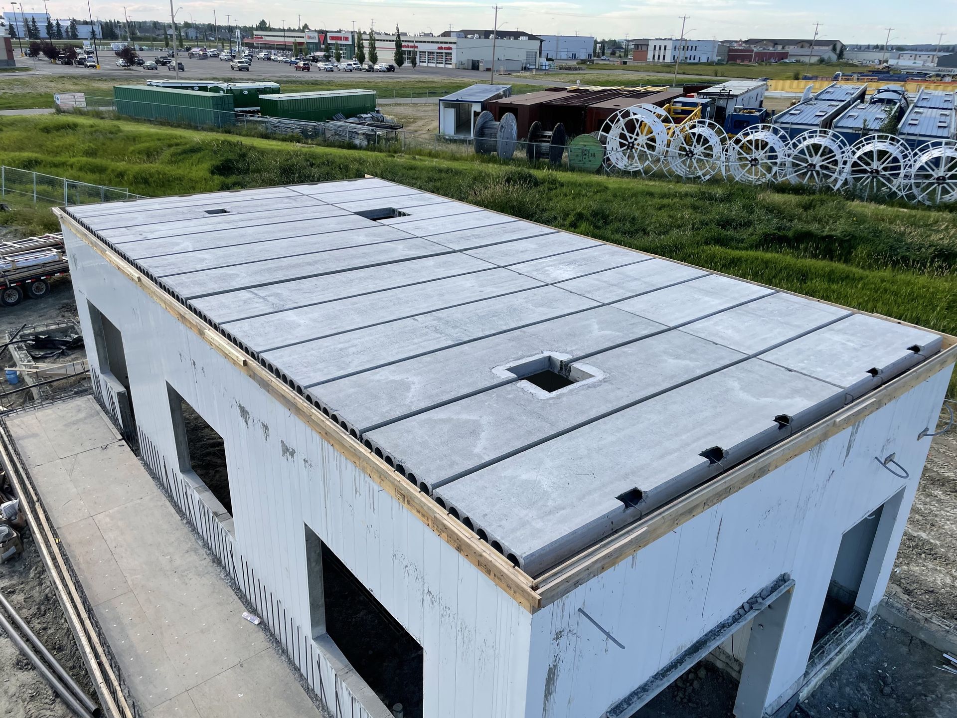 A partially constructed building with concrete walls and roof panels, set in a grassy industrial area.