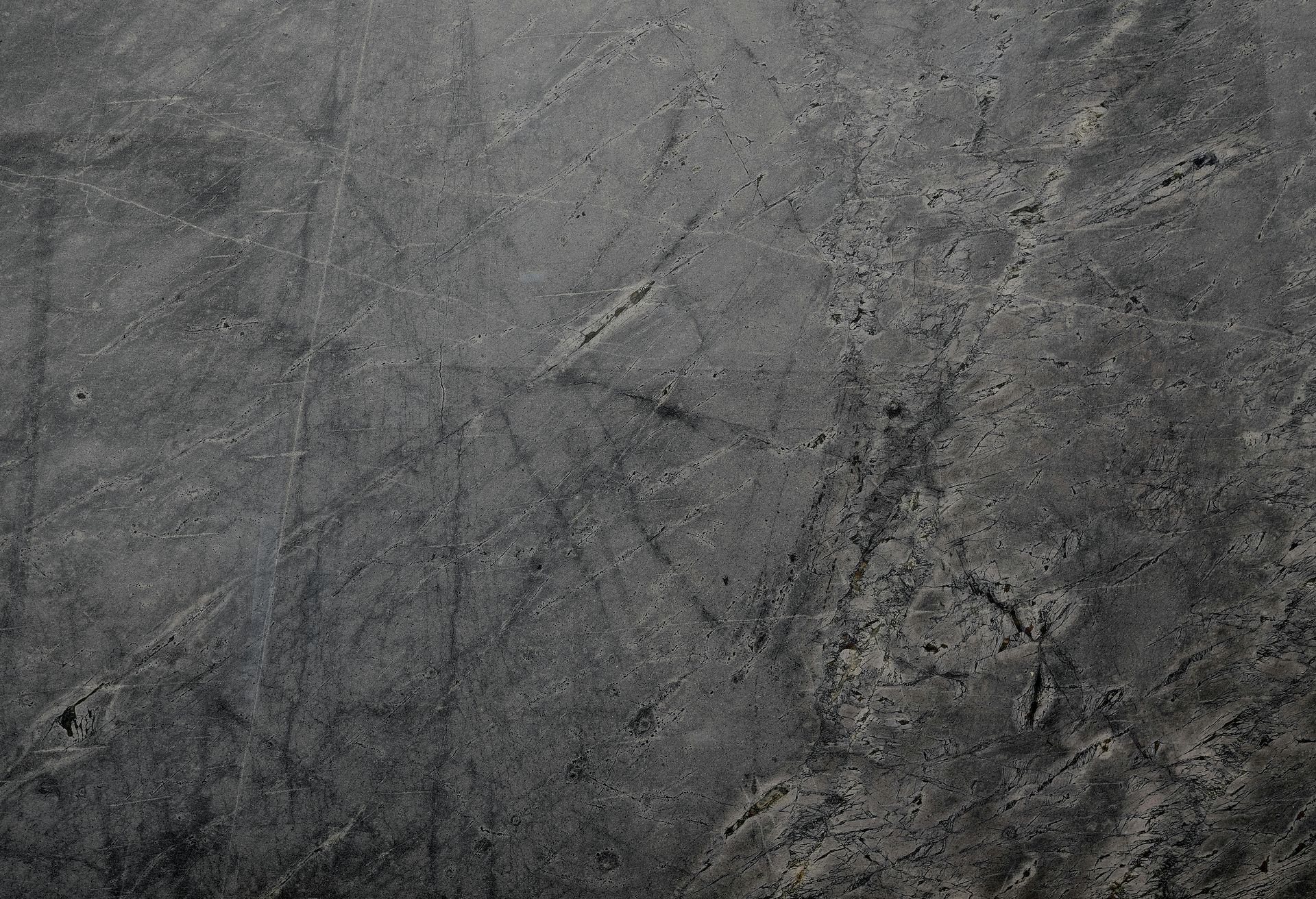 Dark gray, textured concrete surface with subtle variations in tone and visible scratches.