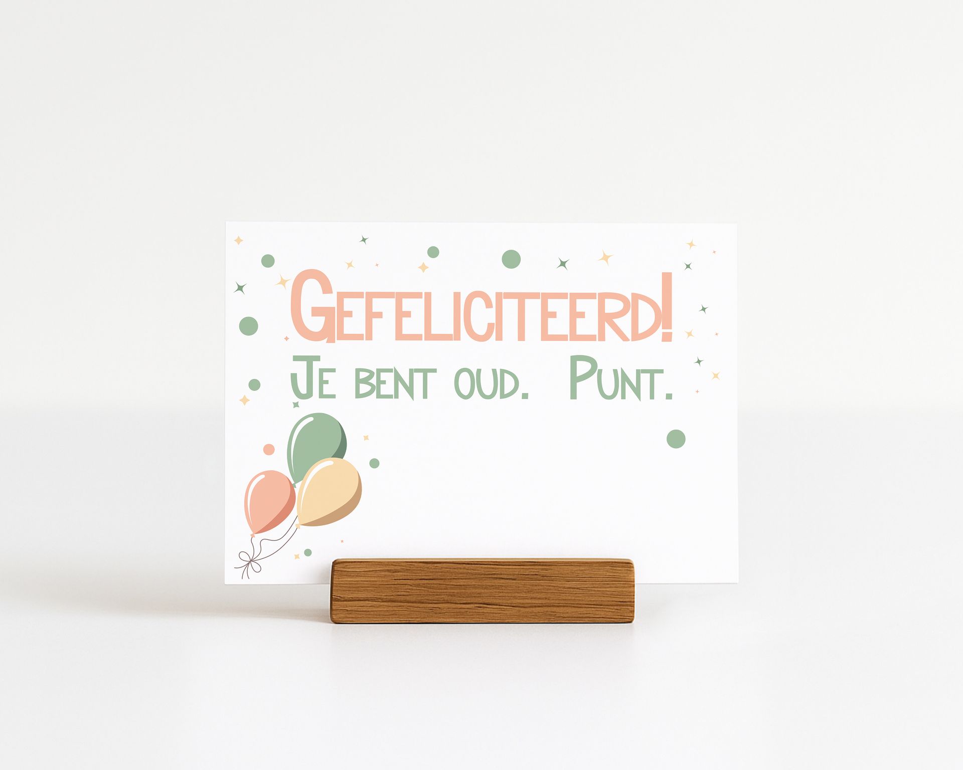 Birthday card with text "Gefeliciteerd! Je bent oud. Punt." on a wooden holder, balloons.