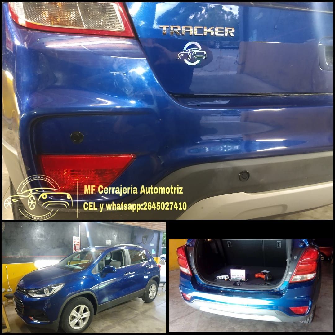 Mecánico con mascarilla instalando un sensor del parachoques trasero en un coche gris en un taller.