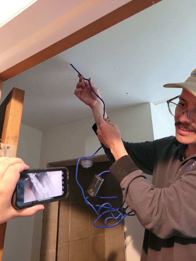 A man is holding a wire while another person takes a picture with a cell phone