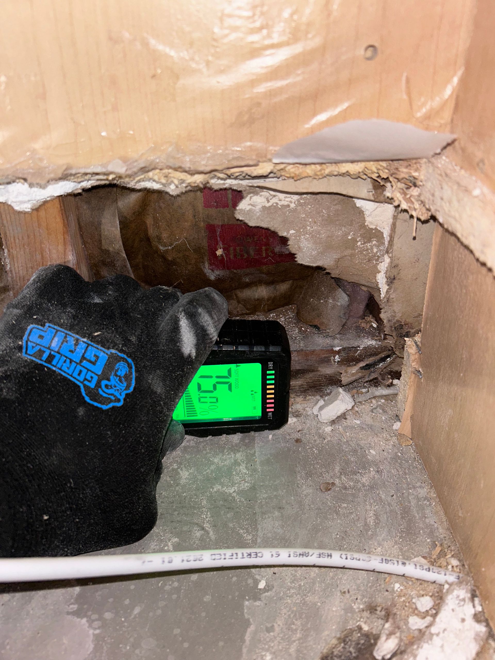 A person is holding a digital thermometer in a hole in the wall.