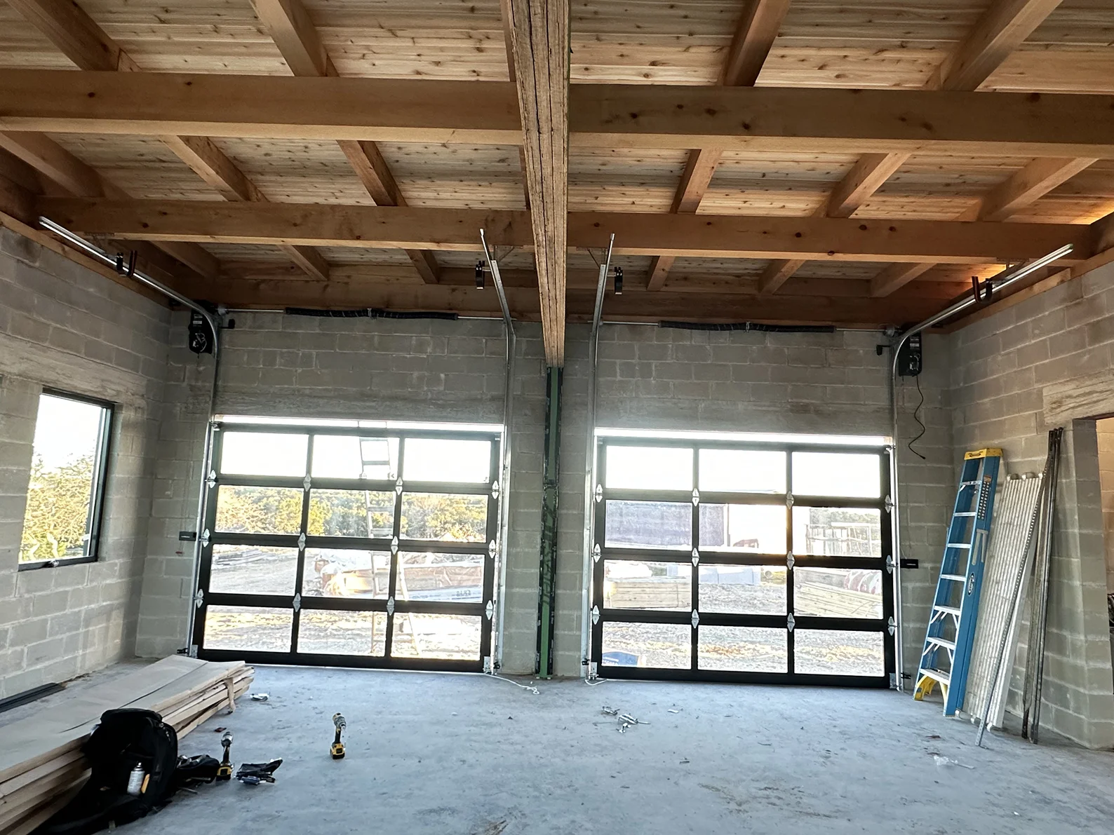 A large empty room with two garage doors and a wooden ceiling.