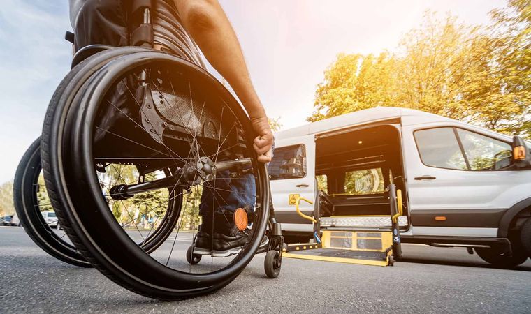 Person in a wheelchair beside a white van at sunset, with a bicycle wheel in the foreground