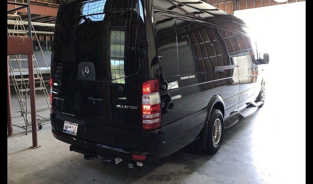 Black cargo van parked under a roof in a garage, viewed from the rear-left side.