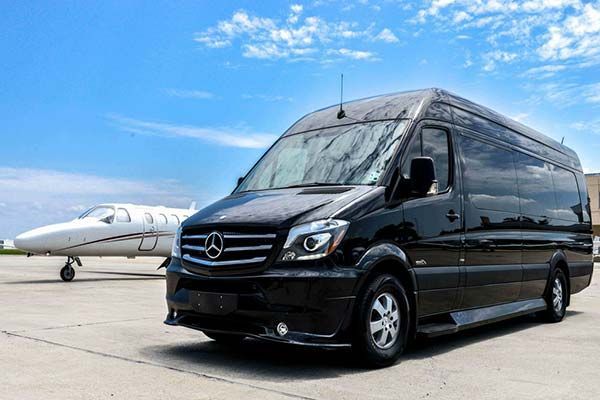 Black Mercedes van parked beside a white private jet on an airport tarmac under a blue sky