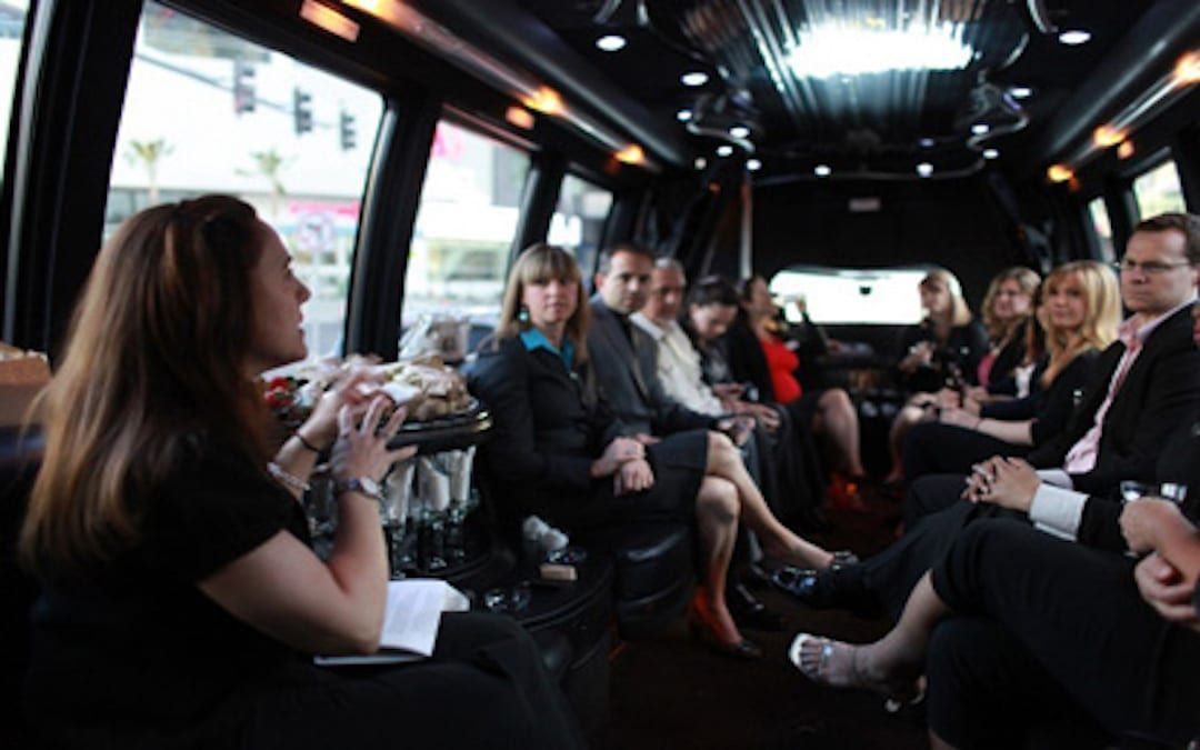 People seated and chatting inside a dimly lit bus or shuttle with large windows.