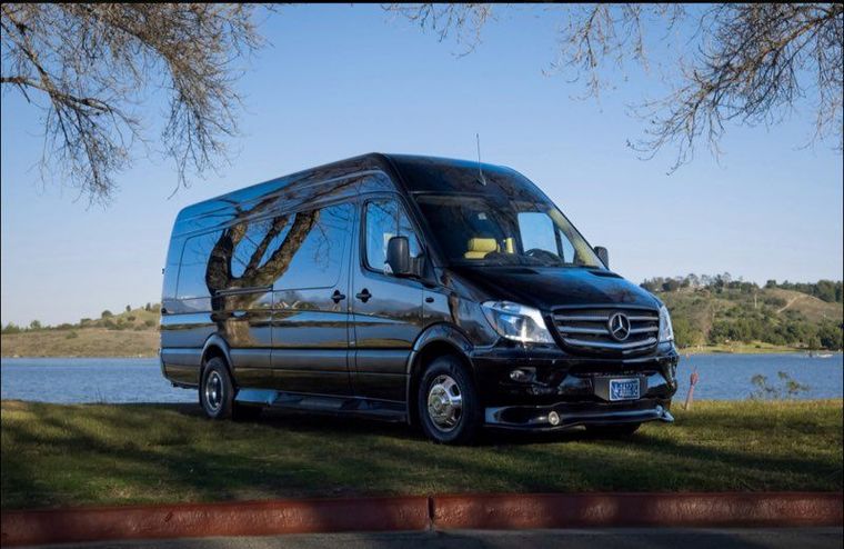 Person in a wheelchair beside a white van at sunset, with a bicycle wheel in the foreground