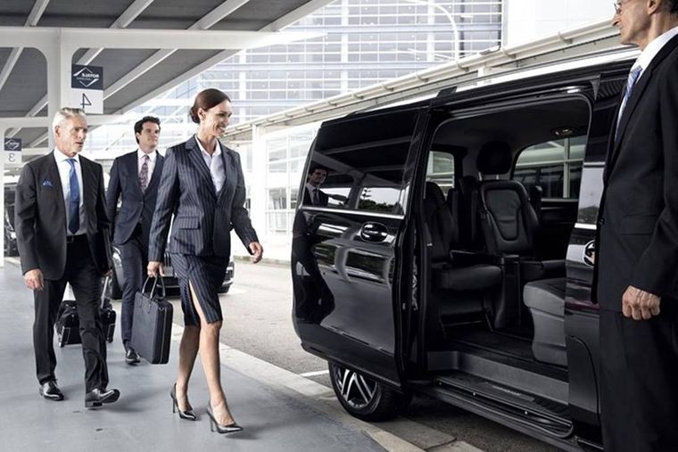 Businesspeople in suits arriving at a black luxury van outside a modern building