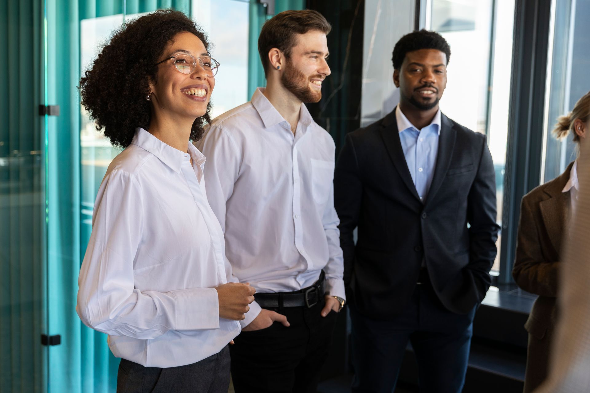 Three professionals standing and smiling in a bright office hallway