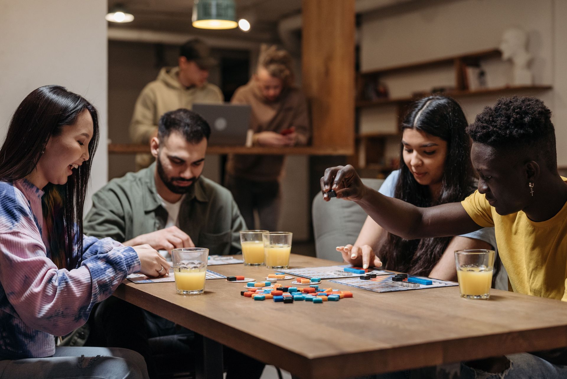 Friends playing a board game at a wooden table with drinks in a cozy indoor room