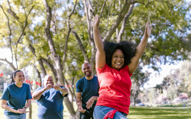 People celebrating outdoors in a park, with one person in a red shirt raising both arms.