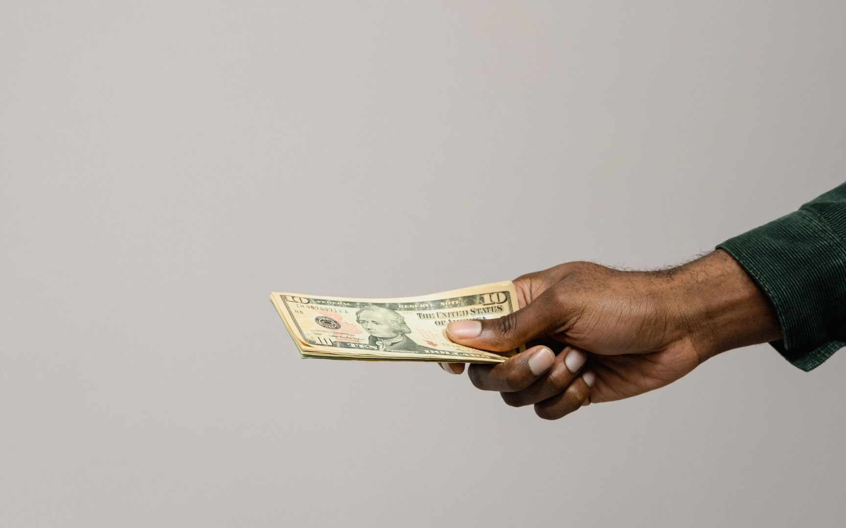 Hand holding a folded dollar bill against a plain gray background
